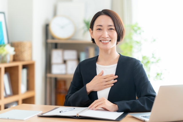 デスクでノートパソコンを前に安心した表情を見せる女性不動産スタッフ