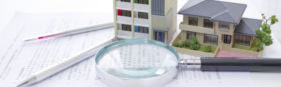 虫眼鏡と書類の上に置かれたマンションと戸建ての模型による不動産調査のイメージ