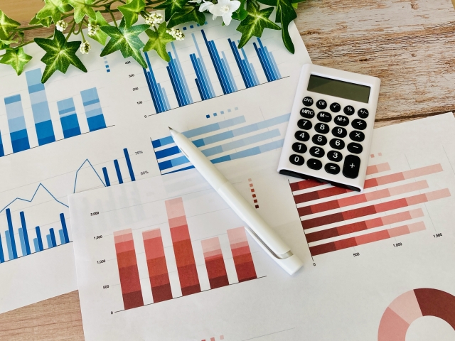 棒グラフや円グラフが印刷された資料と電卓による不動産市場データ分析のイメージ
