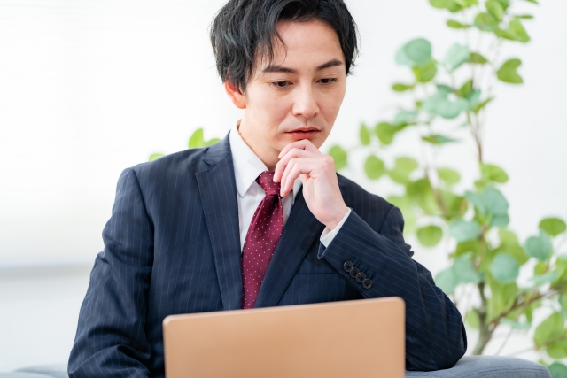 ノートパソコンの画面を見ながら考え込むスーツ姿のビジネスマン