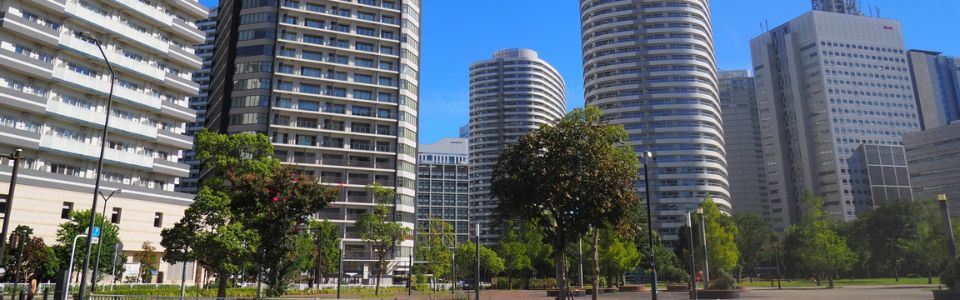 緑の並木道沿いに立ち並ぶ高層タワーマンション群と青空