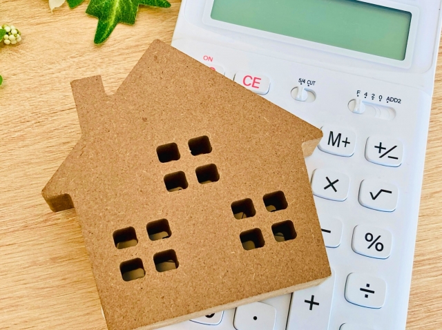 木製の家の模型と電卓を並べた不動産価格査定のイメージ